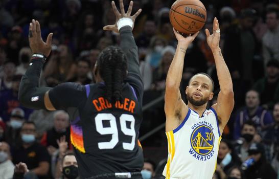 El base de los Warriors de Golden State Stephen Curry lanza el balón sobre el alero de los Suns de Phoenix Jae Crowder en el encuentro del sábado 25 de diciembre del 2021. (AP Photo/Rick Scuteri)