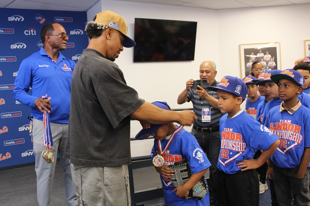 Francisco Lindor, estelar torpedero de los Mets de Nueva York, coloca la medalla a uno de los niños.