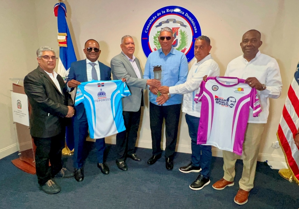 Roberto Rojas, Pedro Pablo Pérez y el cónsul Jesús –Chu- Vásquez, portan la antorcha que el sábado pasado inició su recorrido, mientras miembros del comité organizador y dirigentes deportivos, exhiben las franelas que usarán los atletas.
