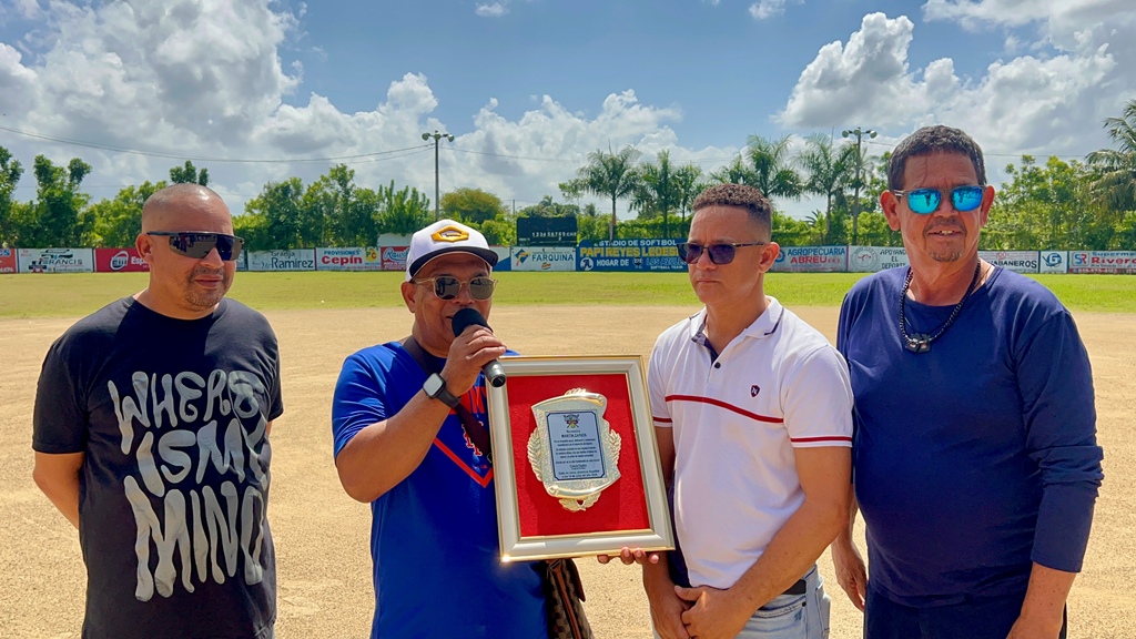 Martín Zapata recibe una placa de reconocimiento de manos de Francis Paulino y directivos del Clásico de Softbol Chata 50 y Más, durante la ceremonia de apertura celebrada en la provincia Espaillat, en homenaje a su destacada trayectoria en el periodismo deportivo.