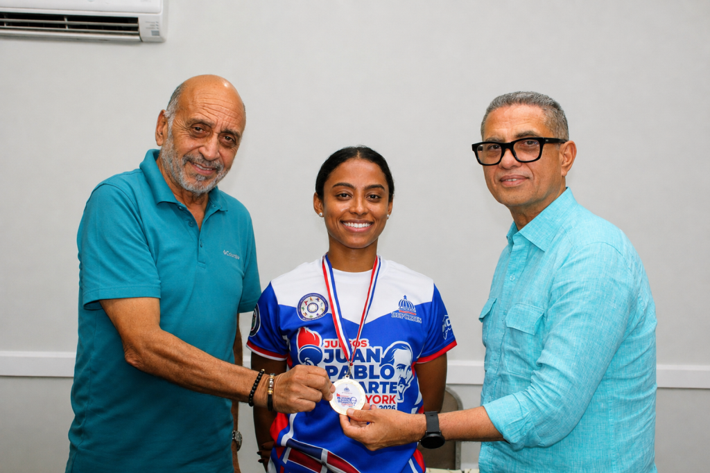 Fernando Teruel y Kennedy Vargas, viceministros de Deportes, colocan la medalla de oro a la campeona Yasiris Ortiz, tras su triunfo en la categoría Élite del torneo de tenis de mesa de los II Juegos Juan Pablo Duarte.